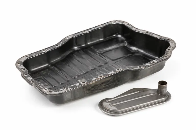 Used automatic transmission oil pan with its fluid filter beside it, on a white background