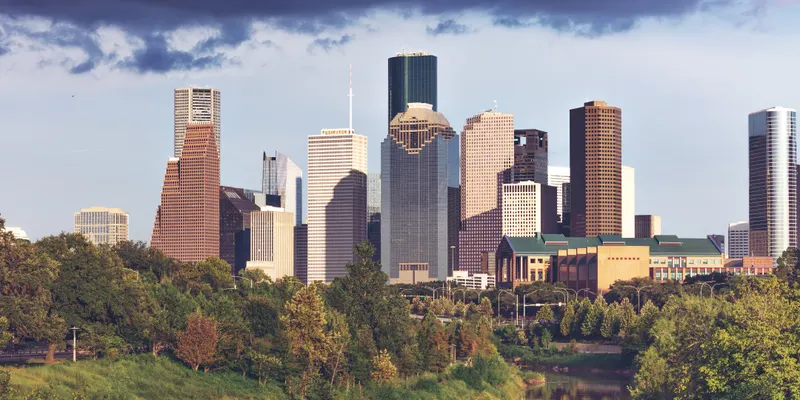 Downtown Houston skyscrapers seen from the west across Buffalo Bayou, with green trees in the foreground