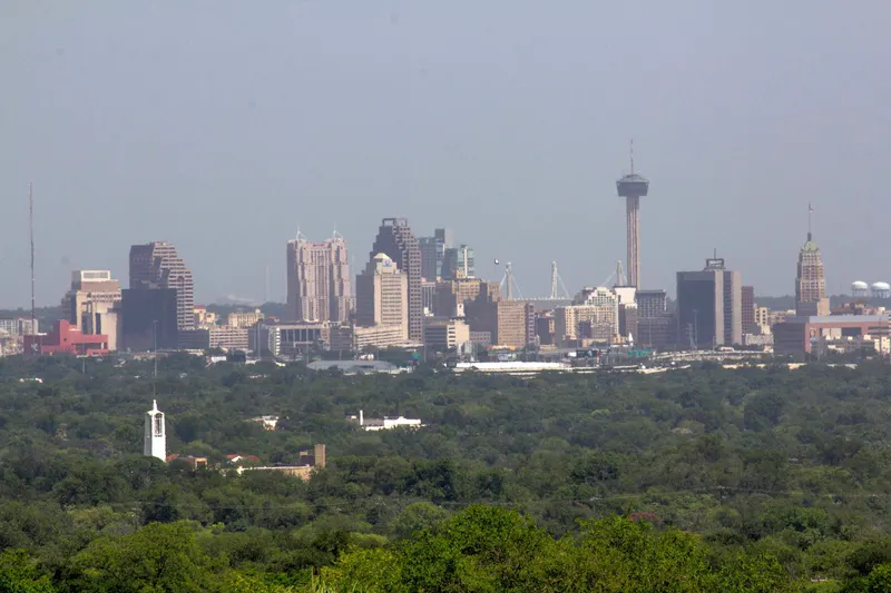 San Antonio skyline with the Tower of the Americas rising above downtown, seen across a wide band of green trees